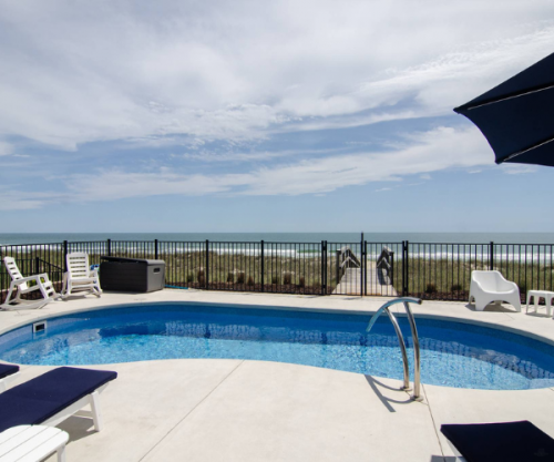 Outdoor pool with a view of the beach and ocean from a vacation rental home.