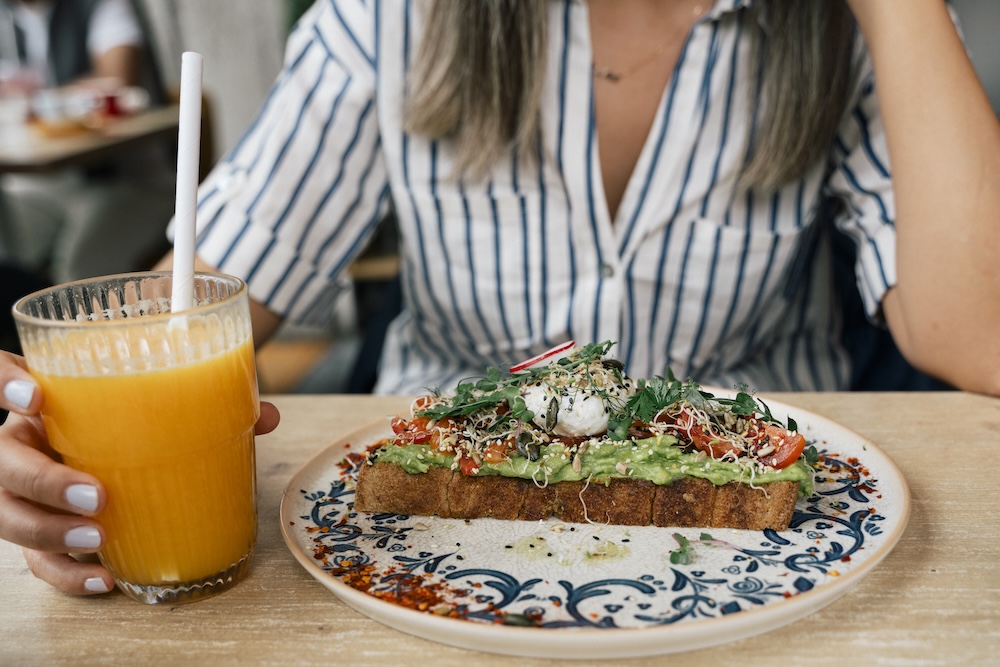 woman at restaurant enjoying orange juice and avocado toast for breakfast 